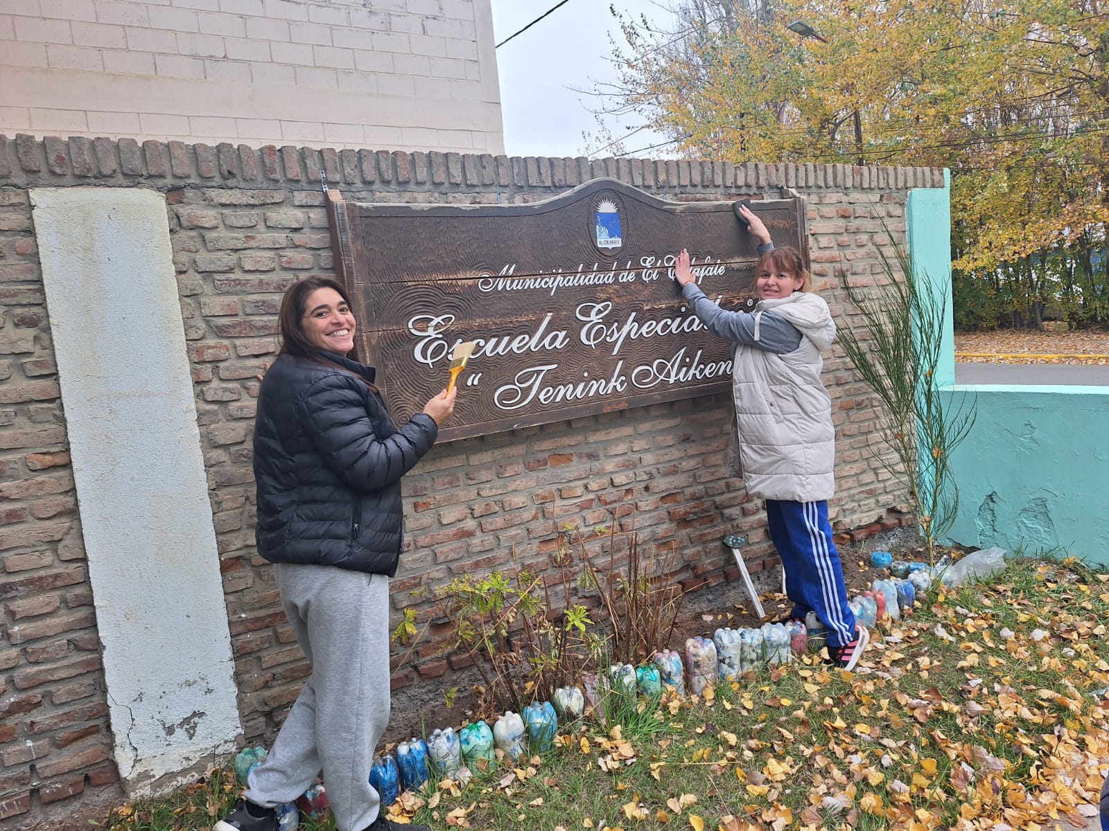 Docentes pintando el cartel de la escuela
