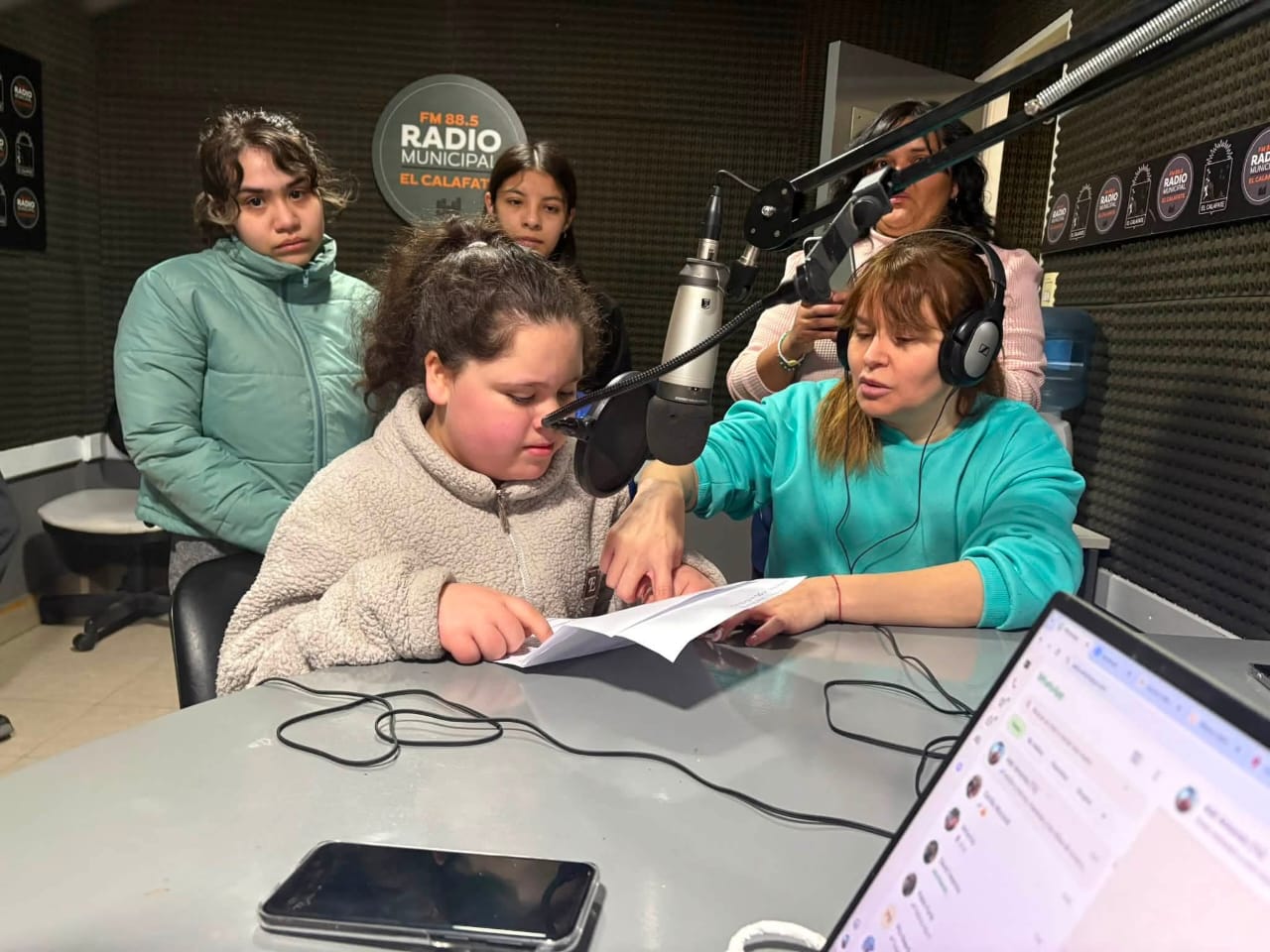 Estudiante leyendo un texto frente al micrófono acompañada por su docente